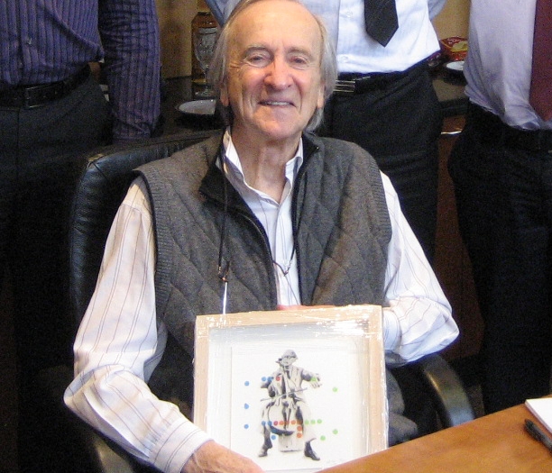 Person seated at a table, holding a framed picture featuring an artistic representation with colourful dots, while others are partially visible in the background