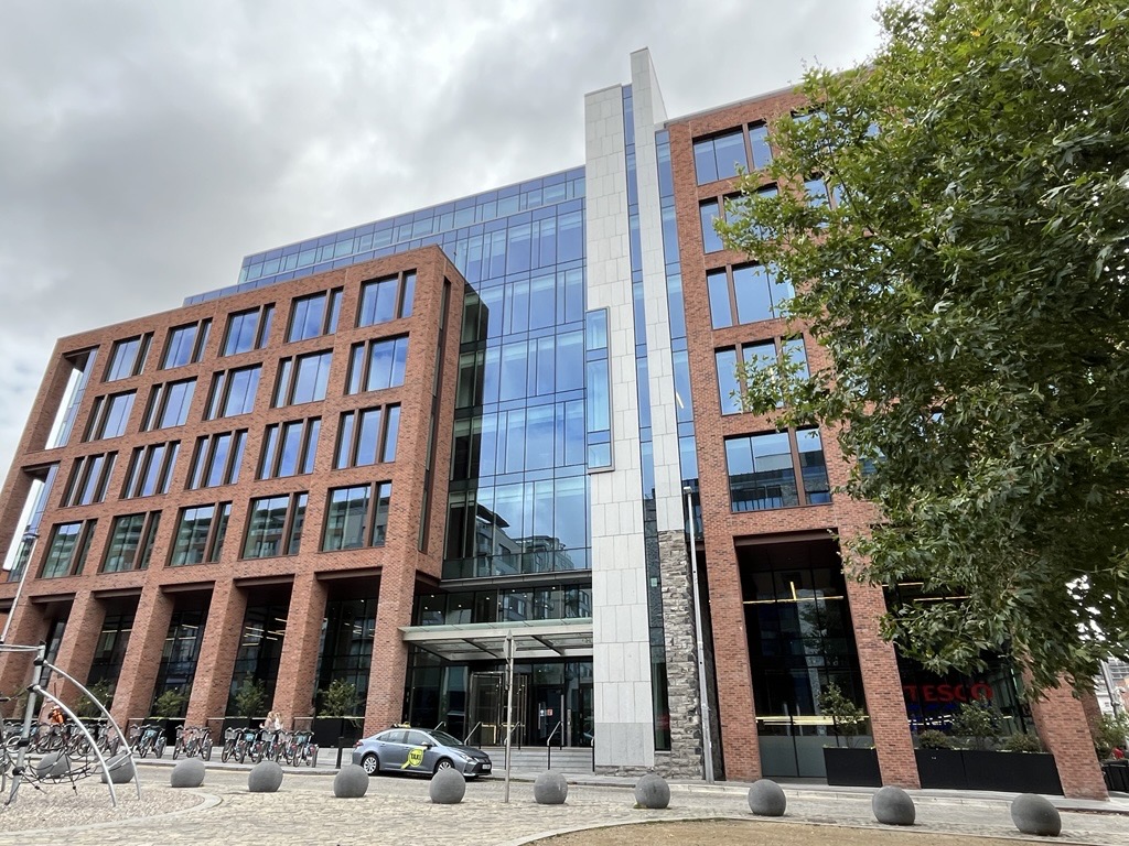 Exterior of a multi‑storey commercial building with red brick facades, large glass sections, and an entrance canopy.