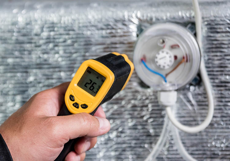 Technician using an infrared thermometer to measure surface temperature on insulated HVAC ductwork during airside system balancing