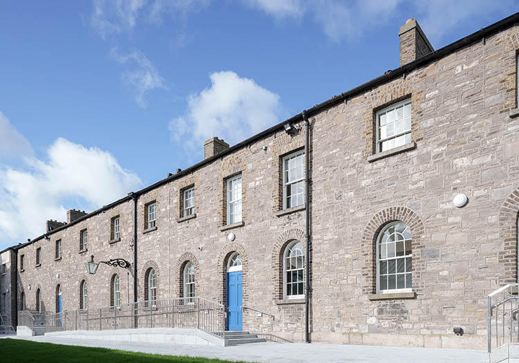 Stone industrial building with arched windows and blue entrance doors under a clear sky.